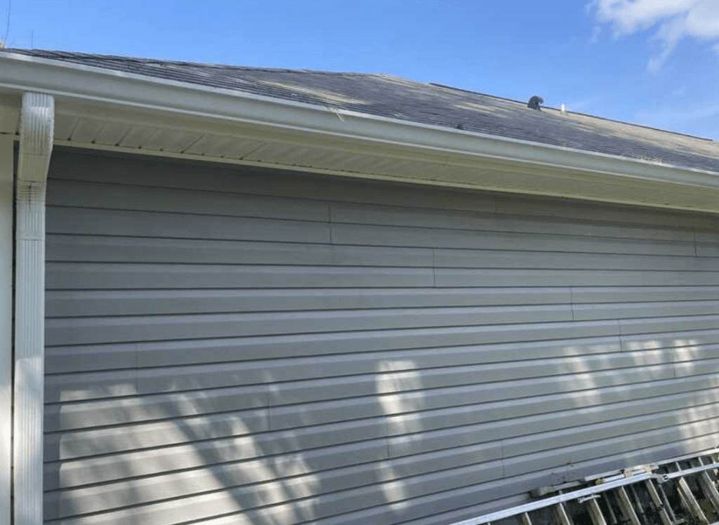 Clean grey vinyl siding with white gutters and dark shingle roofline